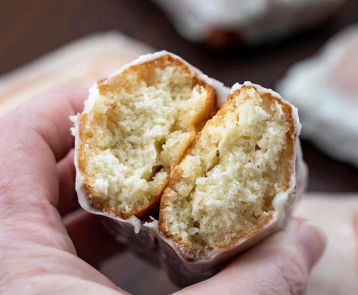 Donut sticks, also known as donut fries, are rectangles of fried dough and are the perfect snack for any donut lover. Dip them in a glossy glaze for a classic treat, or get creative and roll them in cinnamon and sugar, dust them with confectioners' sugar, or even add your favorite sprinkles or chopped nuts. I will also let you know how you can make these in the oven and an air fryer. Hand Holding broken in half donut stick showing texture inside.