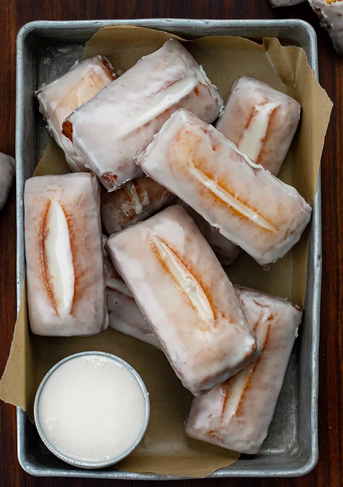 Donut sticks, also known as donut fries, are rectangles of fried dough and are the perfect snack for any donut lover. Dip them in a glossy glaze for a classic treat, or get creative and roll them in cinnamon and sugar, dust them with confectioners' sugar, or even add your favorite sprinkles or chopped nuts. I will also let you know how you can make these in the oven and an air fryer. Tray of Glazed Donut Sticks on a Wood Counter.